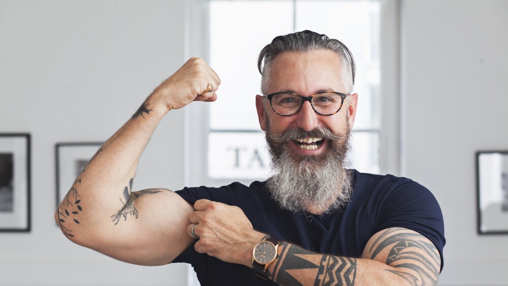 Close up of smiling muscular Caucasian hipster man flexing biceps
