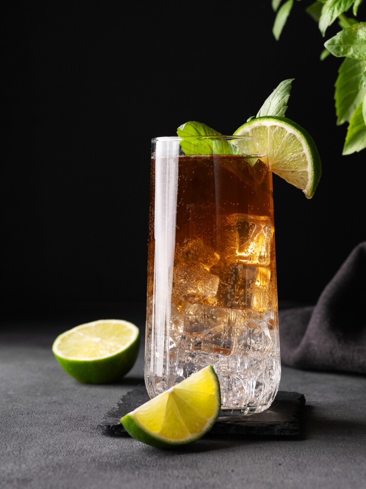 Coffee brew with tonic, ice and lime in a tall glass on a dark background with citrus fruit and herb. Concept craft refreshing trend drink.