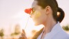 Portrait of young woman with poppy flower in her hand and closed eyes at sunset.