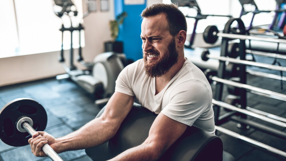 Male Athlete Doing Arm Workout With Barbell In Gym