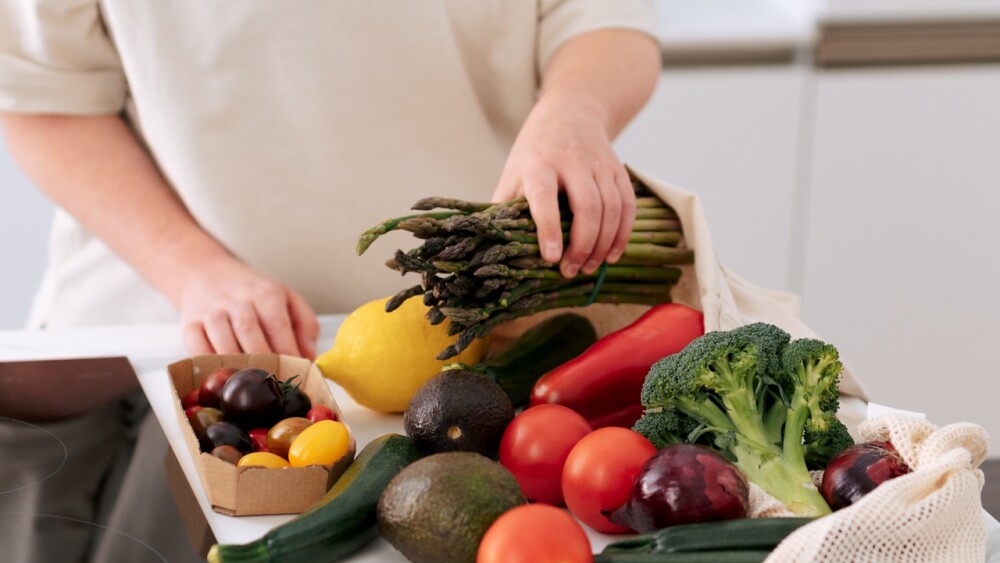 woman takes fresh organic vegetables Zucchini, broccoli, asparagus, bell peppers, tomatoes, lemon. eco textile packaging unpacking grocery in kitchen.