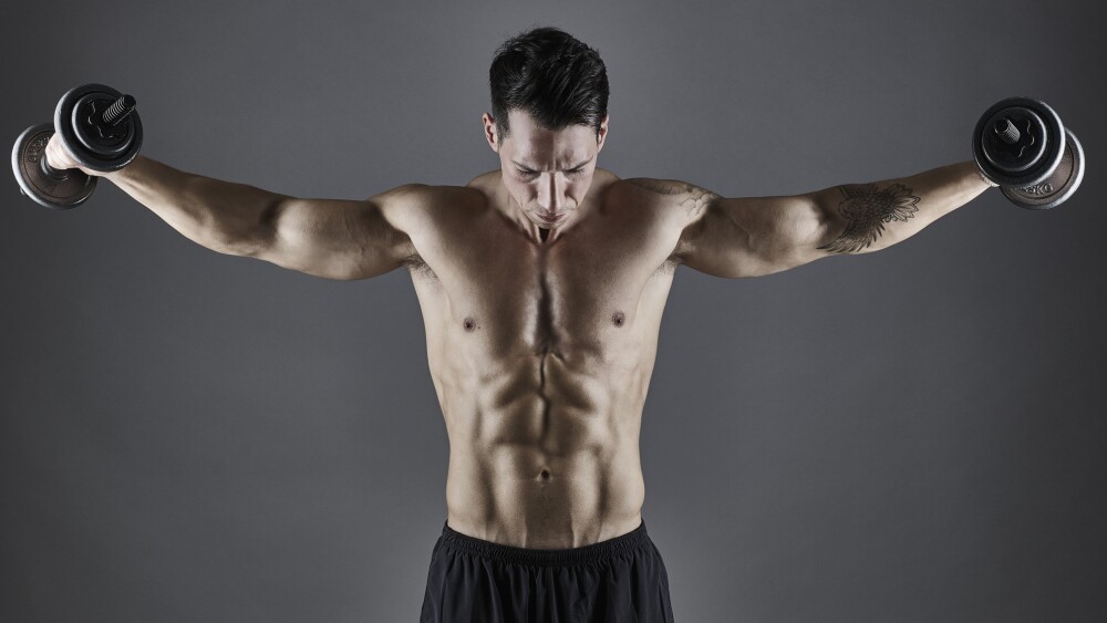 Young athletic male bodybuilder lifting dumbbells